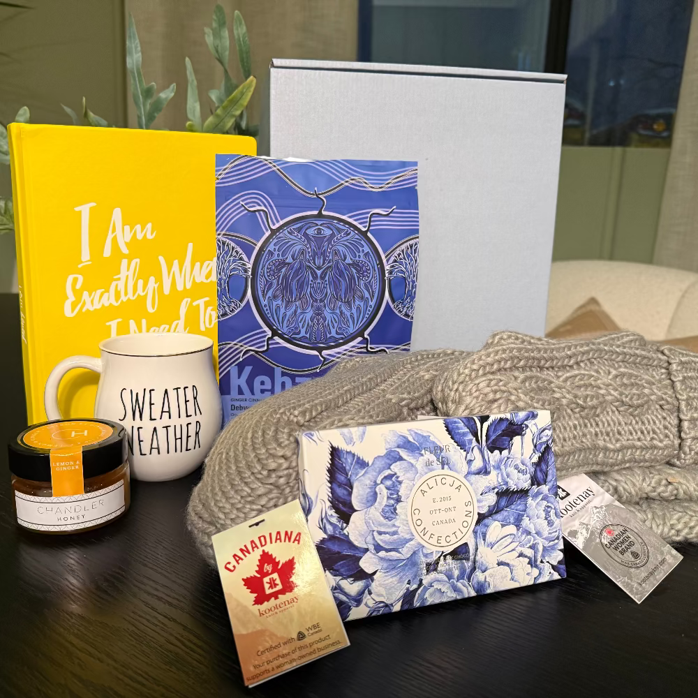 Collection of items including a yellow book, mug, candle, and folded sweater on a dark surface.
