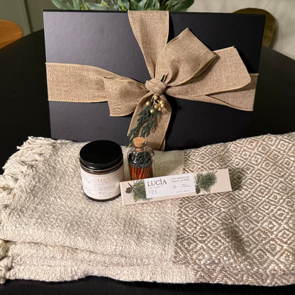 Gift set with black box, candle, and bottle  of matches on a textured blanket