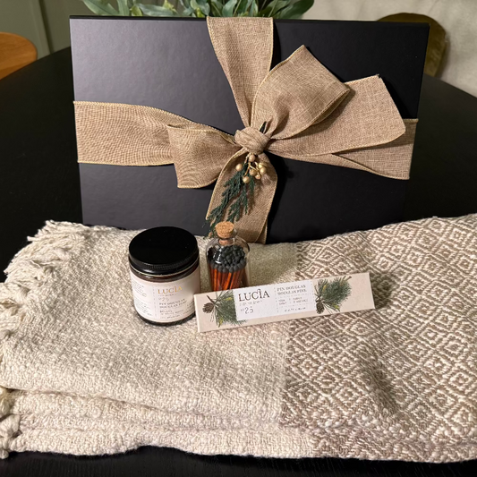 Gift set with black box, candle, and bottle  of matches on a textured blanket